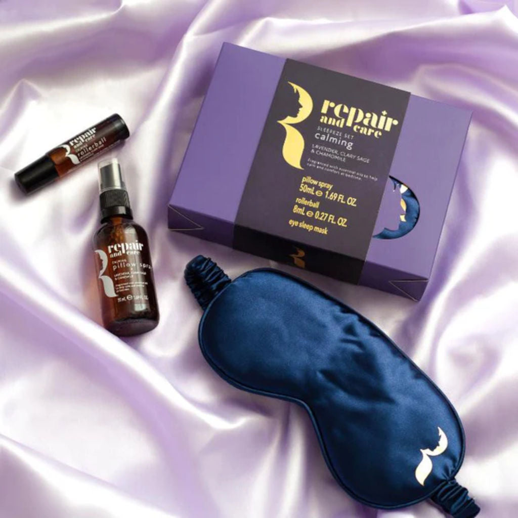 Sleep and self-care products including a sleep mask, eye drops, and a spray bottle on a satin surface.