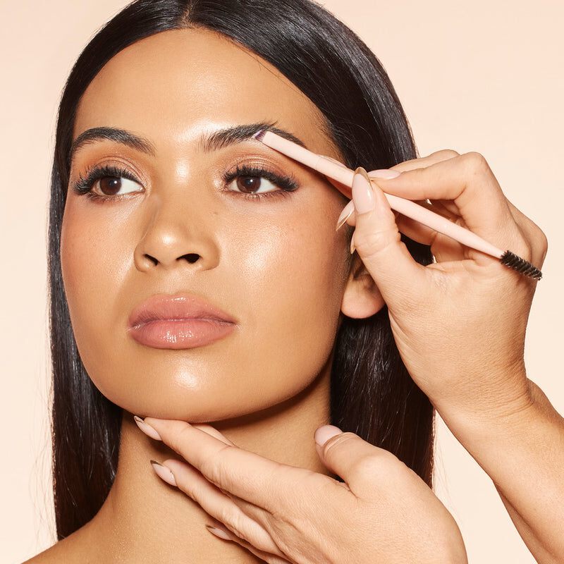 Woman applying makeup with a brush on a beige background