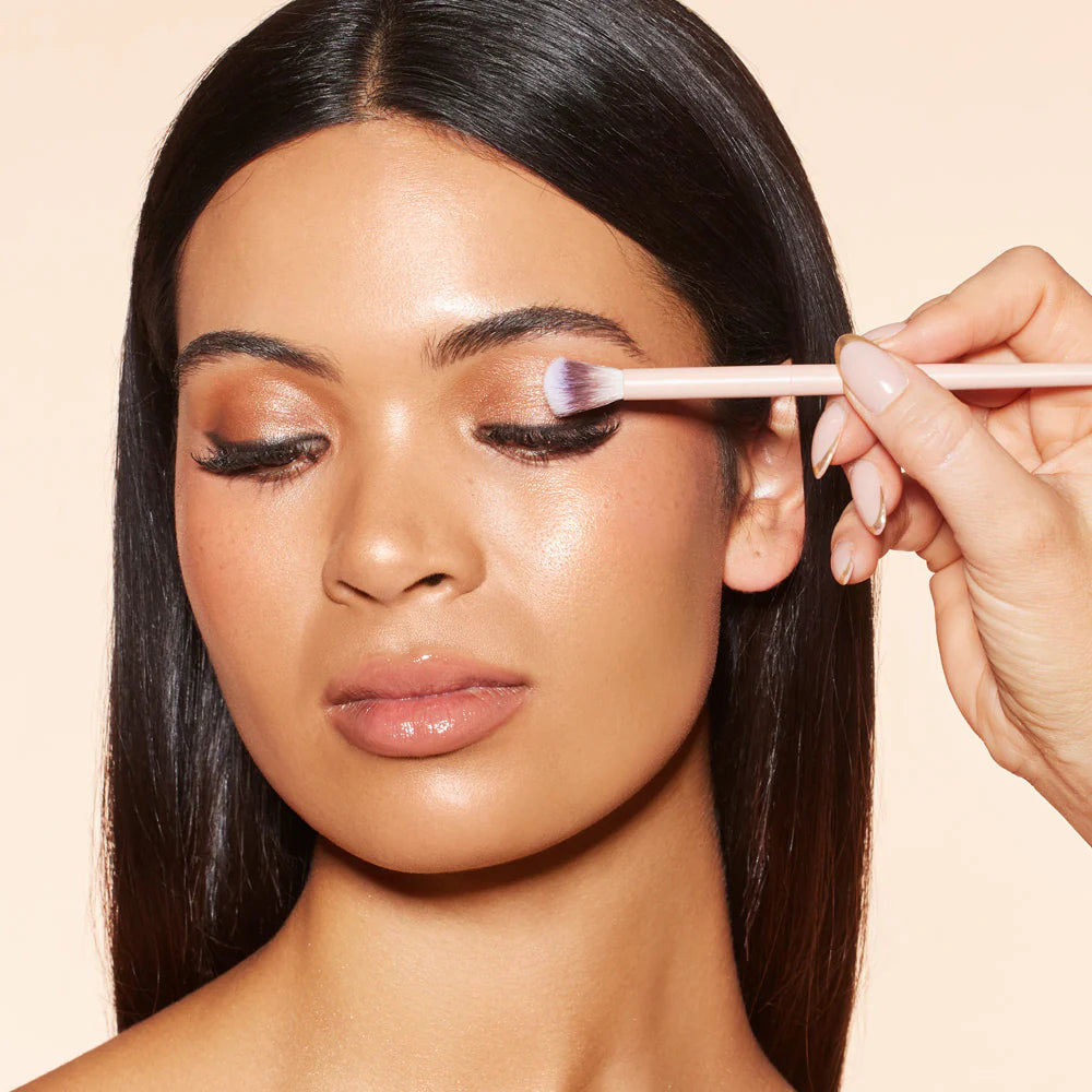 Woman having makeup applied to her eyelid with a brush on a beige background