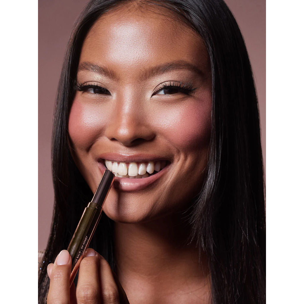 Woman applying lipstick with a brush on a neutral background