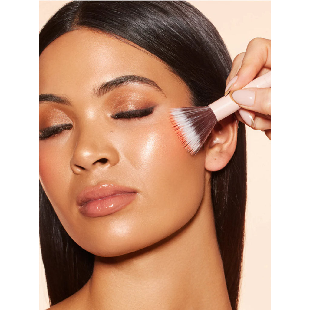 Woman applying makeup with a brush on a beige background
